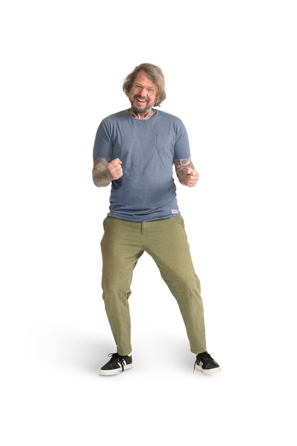 Ein Mann mit Brille, hellblauem Shirt, tätowierten Armen und khakifarbener Hose.