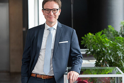 Ein freundlich aussehender Mann im mittleren Alter mit Brille im blauen Anzug.