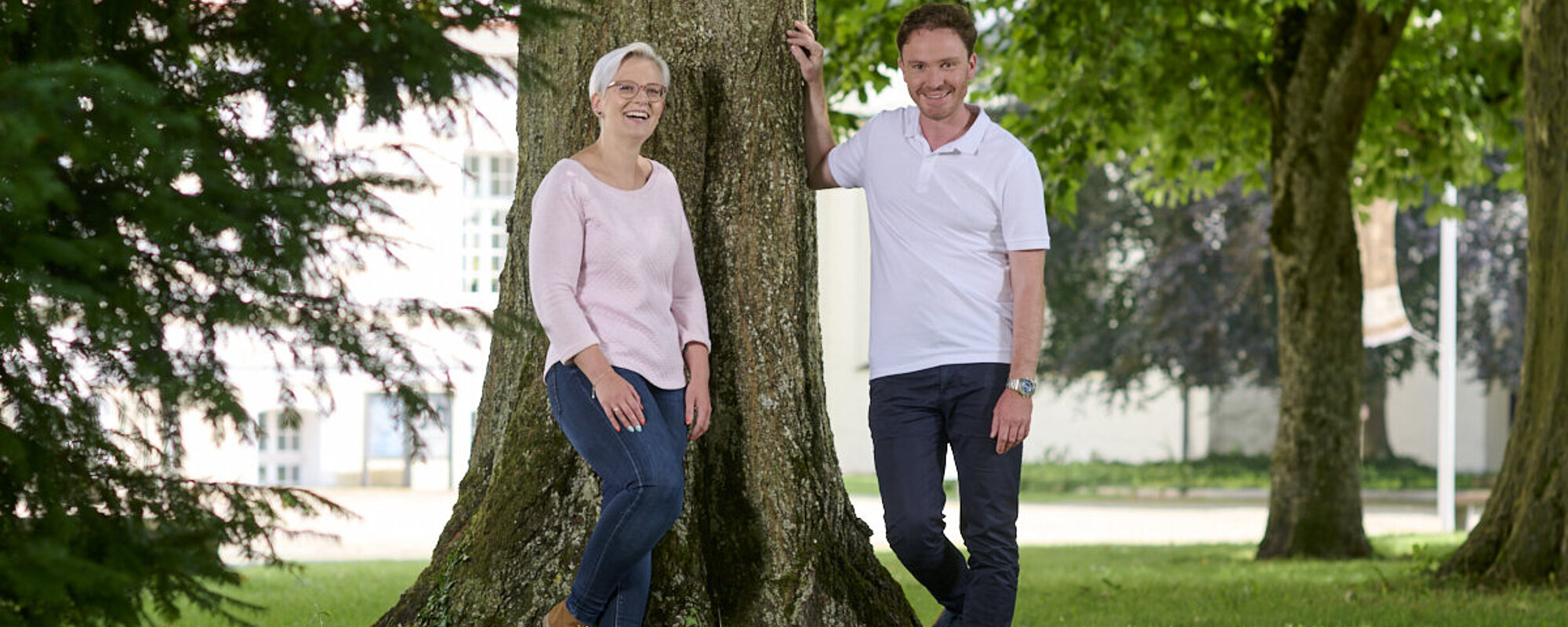 Eine junge Frau und ein Mann im mittleren Alter stehen vor einem großen Baum. 