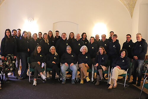 Eine Gruppe von rund 40 Personen sitzt und steht vor einer weißen Wand, alle tragen schwarze Hoodies mit ZfP-Logo.